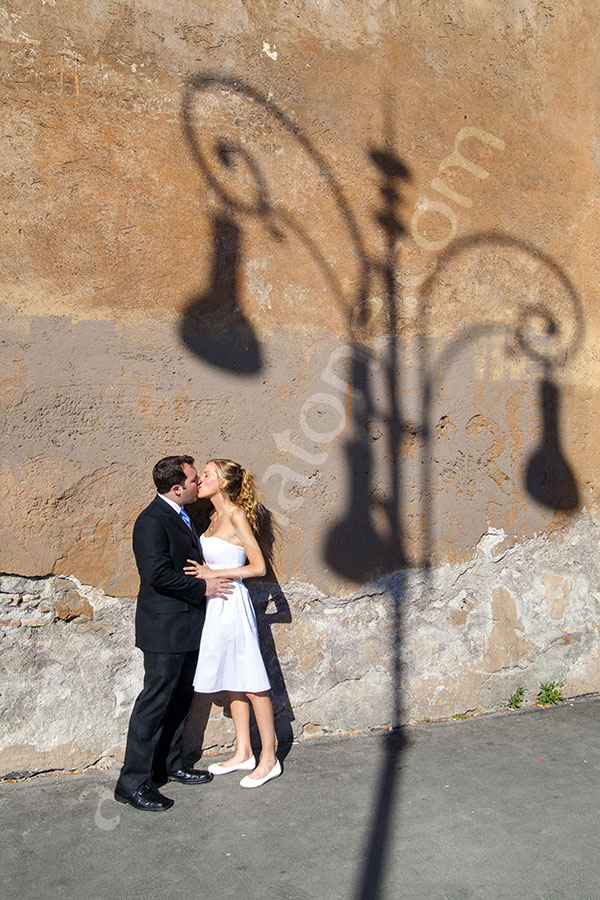 Newlyweds kissing next to the shadow of a light pole onto the street wall