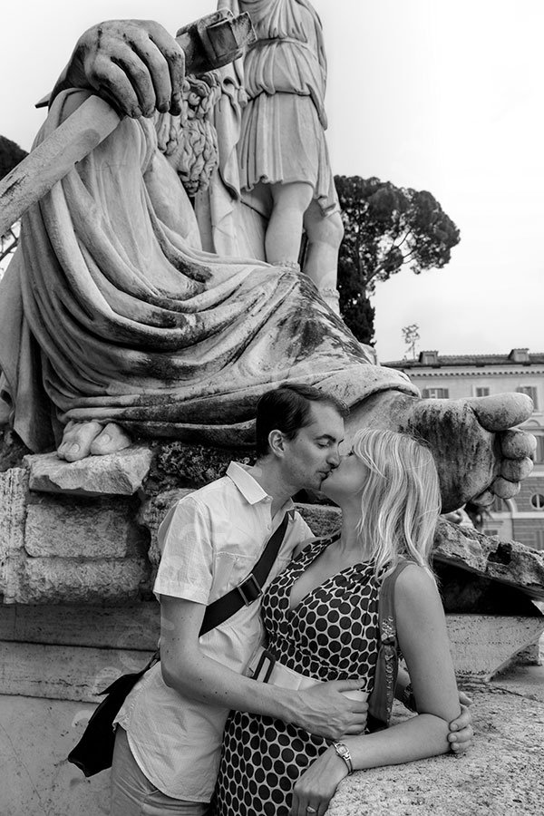 Black and white picture of a couple kissing underneath a statue
