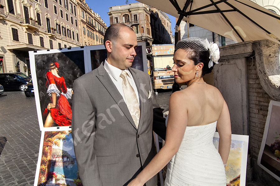 Newlyweds standing among paintings in Piazza Trinita' dei Monti.