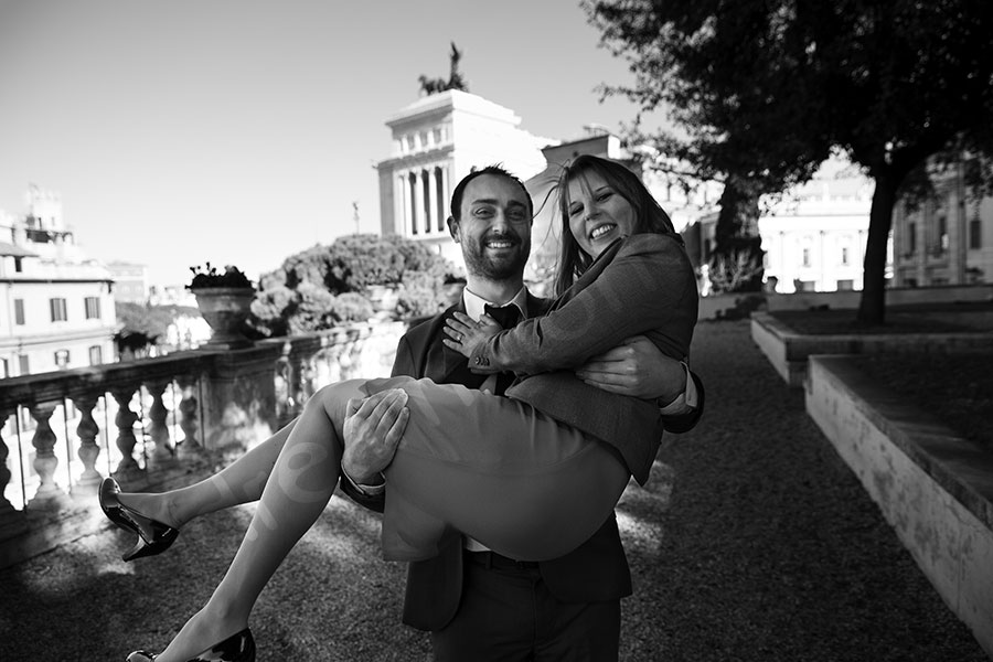 He carries her in his arms with Piazza Venezia in the distance