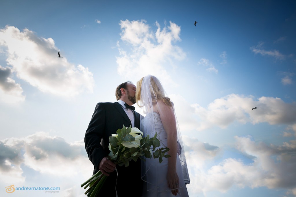 Newlyweds kissing underneath blue sky.