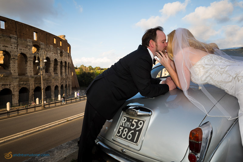 Kissing on a classic vintage car in Rome in front of the Colosseum. Destination wedding photographer Italy.