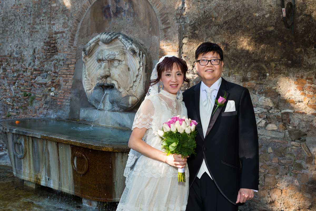 Portrait picture of bride and groom standing in front of a water fountain in the Aranci garden.