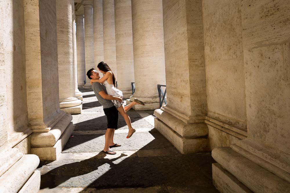 Man picking up a fiancee during a photo shoot underneath the columns of St. Peter's square in the Vatican.