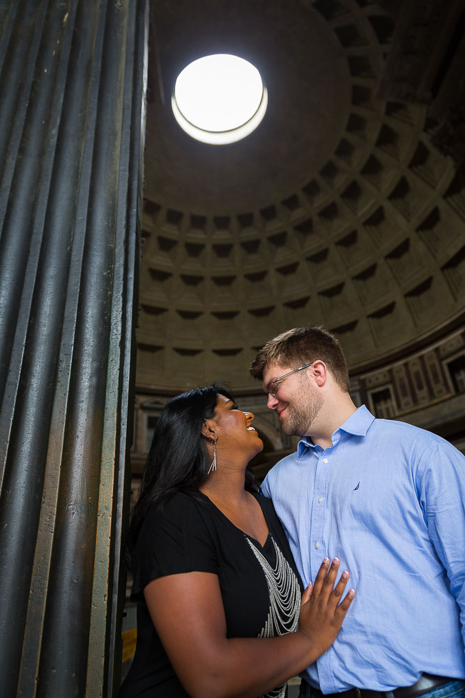 A couple standing at the entrance of the Pantheon with the hole light above.