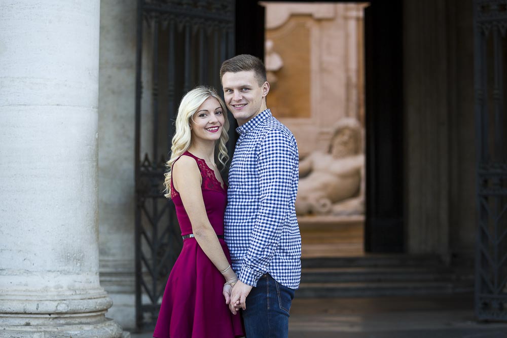 Portrait picture of a couple posing in front of old marble statues.