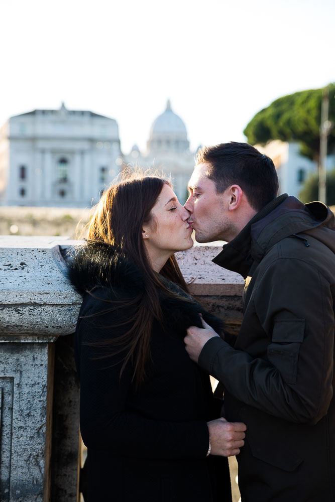 A couple kiss on the bridge of Castel Sant Angelo overlooking the Vatican city in the distance