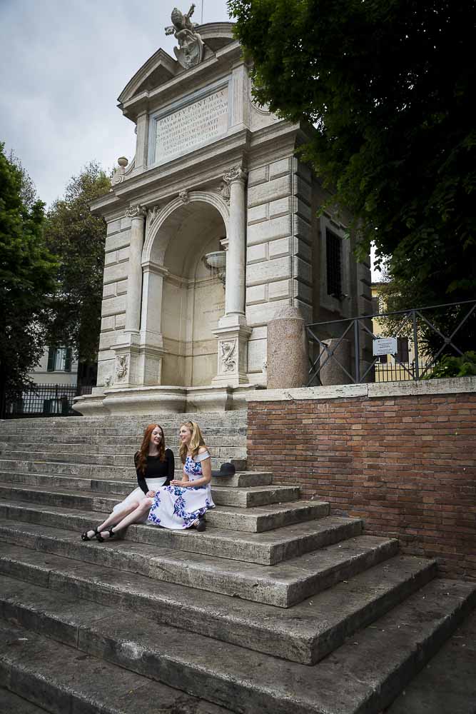 Friends sitting down on stairs that lead to a water fountain in Piazza Trilussa