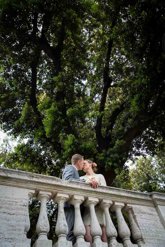 Newlywed couple kissing underneath a tree in Pincio park