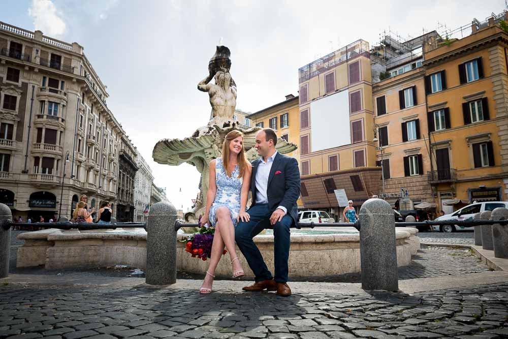 Couple sitting down on the edge of the Triton fountain in Piazza Barberini during an engagement session
