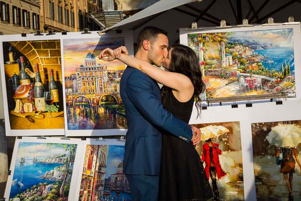 Kissing in Rome during an engagement session photographed next to artist paintings