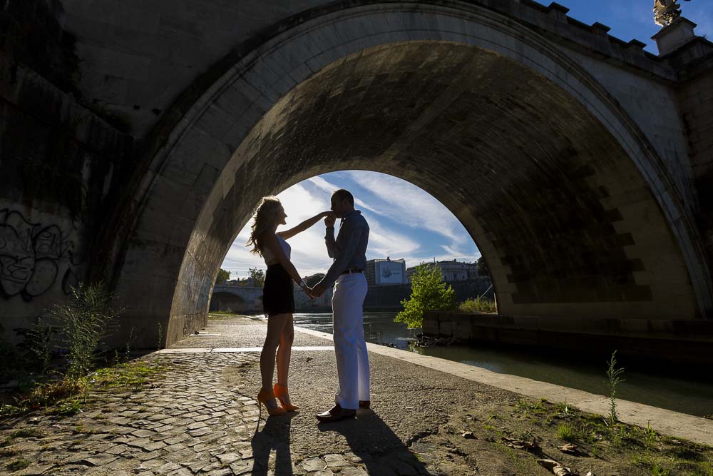 Man kissing fiancee hand in silhouette under the Castel Sant'Angelo bridge 