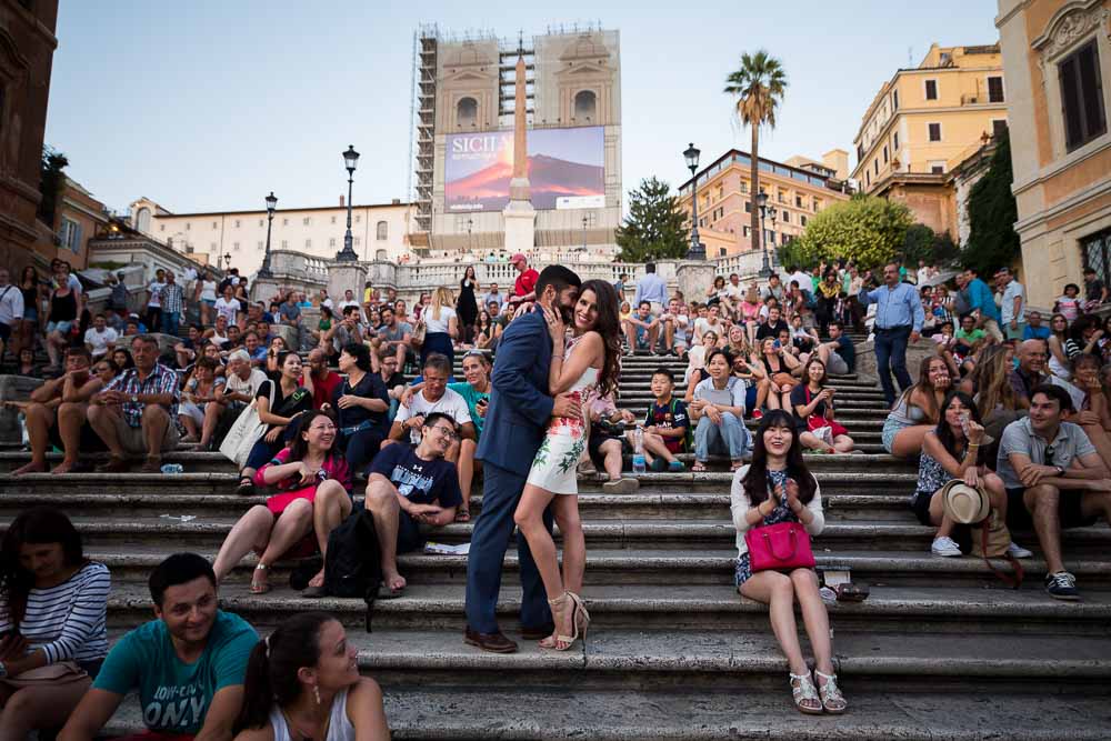 Couple posing in love among a large crowd of tourists sitting down on the stairs of Piazza di Spagna in Rome Italy