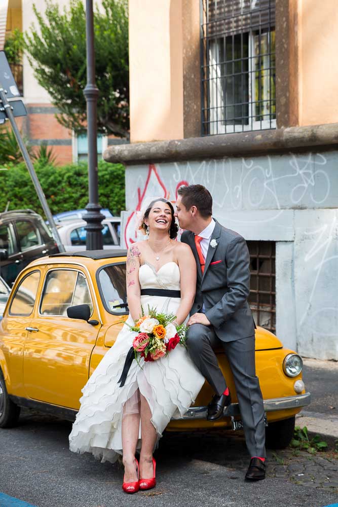 Groom and bride leaning on a yellow fiat 500 parked
