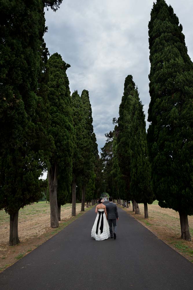 Bride and groom walking together under cypress trees in Italy