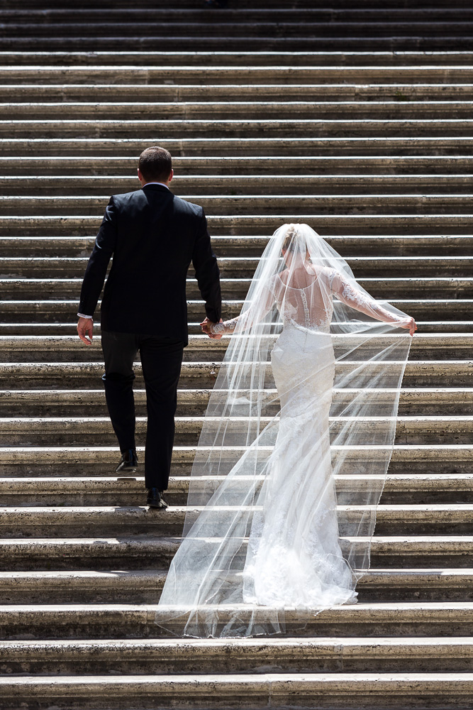 Bride and groom rear picture view as they are ascending stairs. Wedding dress in the air.