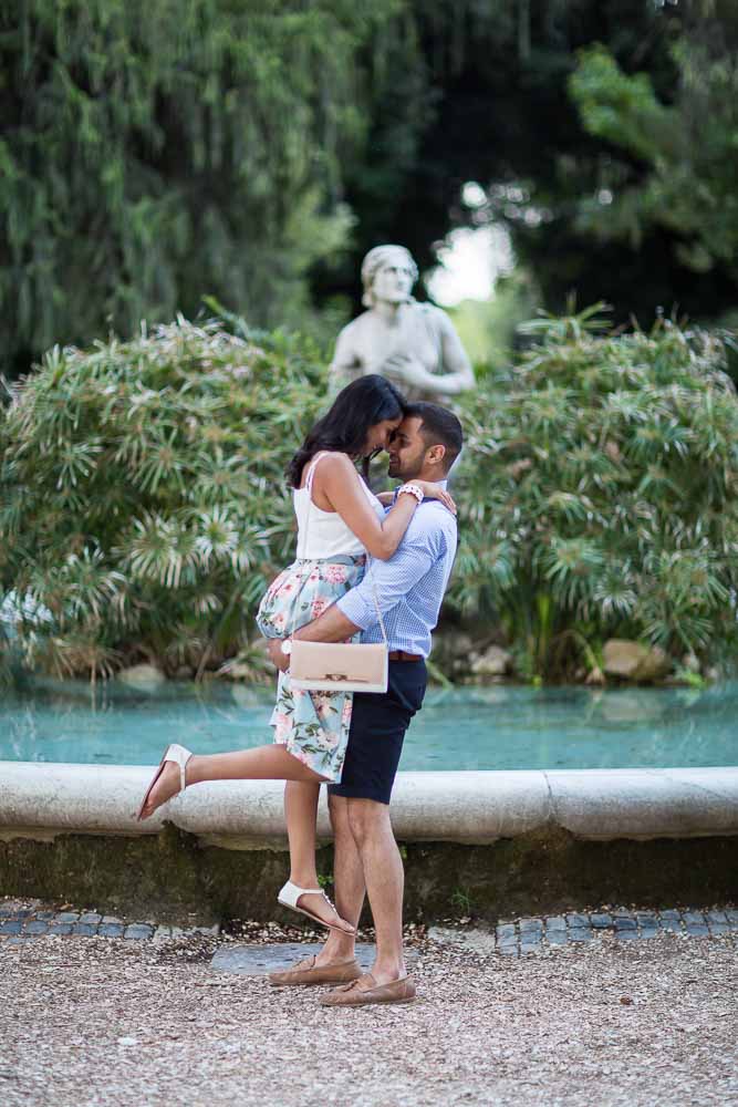 Man picking up fiancee in front of a water fountain