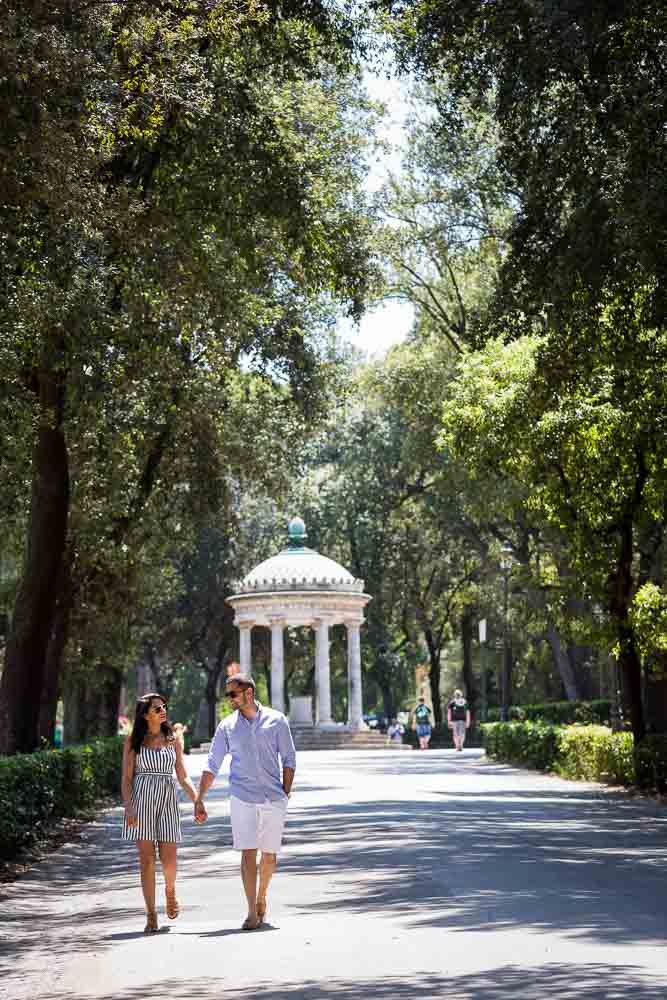 Walking hand in hand in Parco Borghese with a small temple in the background