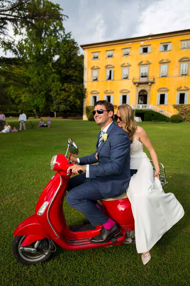 Married and taking a ride on a red Vespa in the Italian Tuscany countryside villa estate. Destination Wedding Photography in Tuscany Pisa 