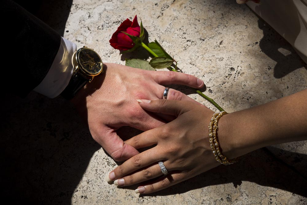 Macro image of a man and woman's hand with engagement rings and a red rose