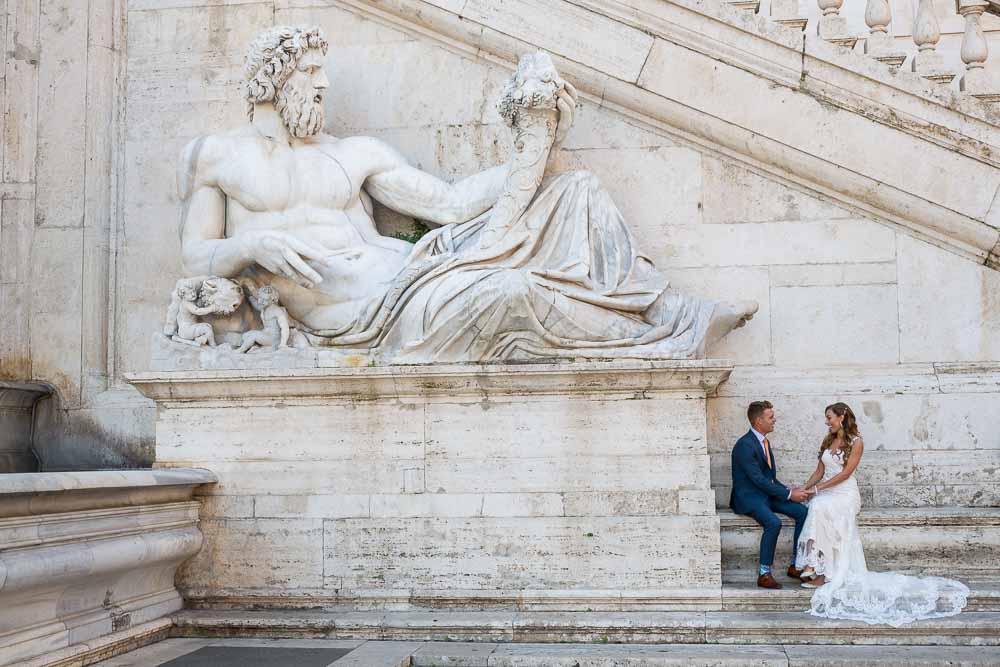 Bride and groom sitting next to a large roman marble statue