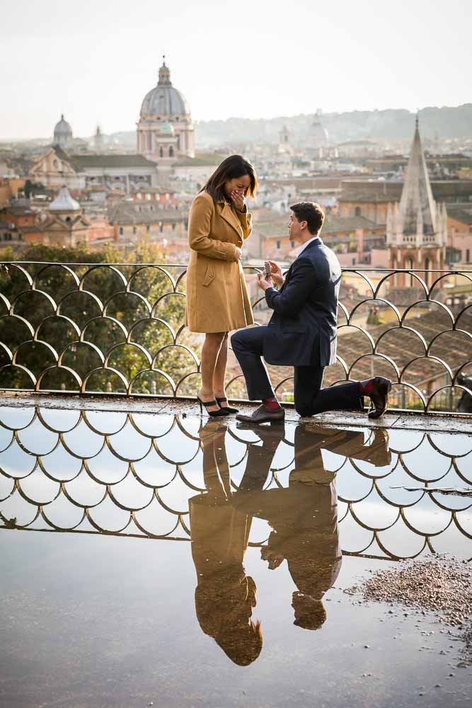 Proposing with one knee down overlooking the city panoramic view from above. And the beautiful water puddle reflection