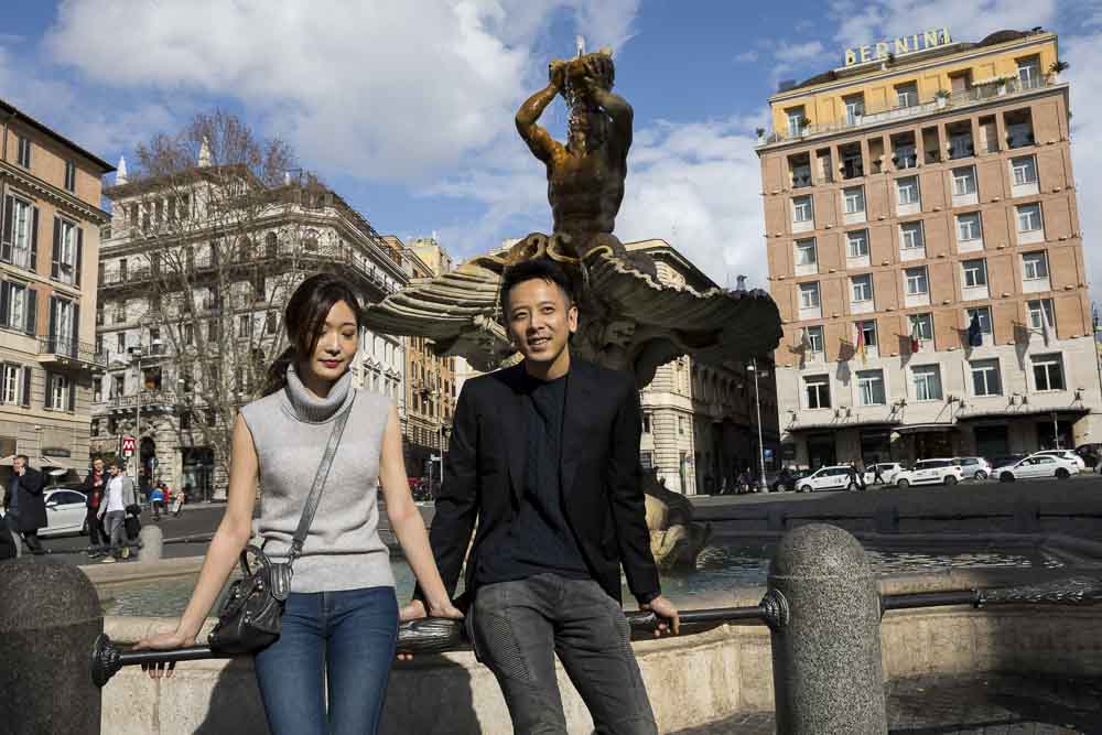 Couple together sitting down by the Bernini water fountain found in Piazza Barberini