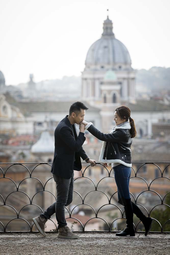 Chivalry moment of man kissing girlfriend's hand. Romance over the Roman rooftops during an engagement photography session in Rome