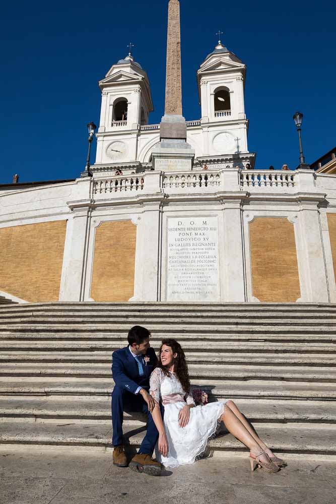Sitting down pose just married couple at the Spanish steps with Church Trinita' dei Monti in the background