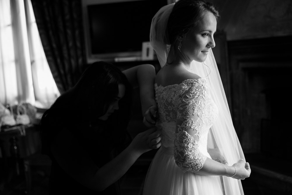 Black and white photography of the bride helped by the bridesmaid getting dress done