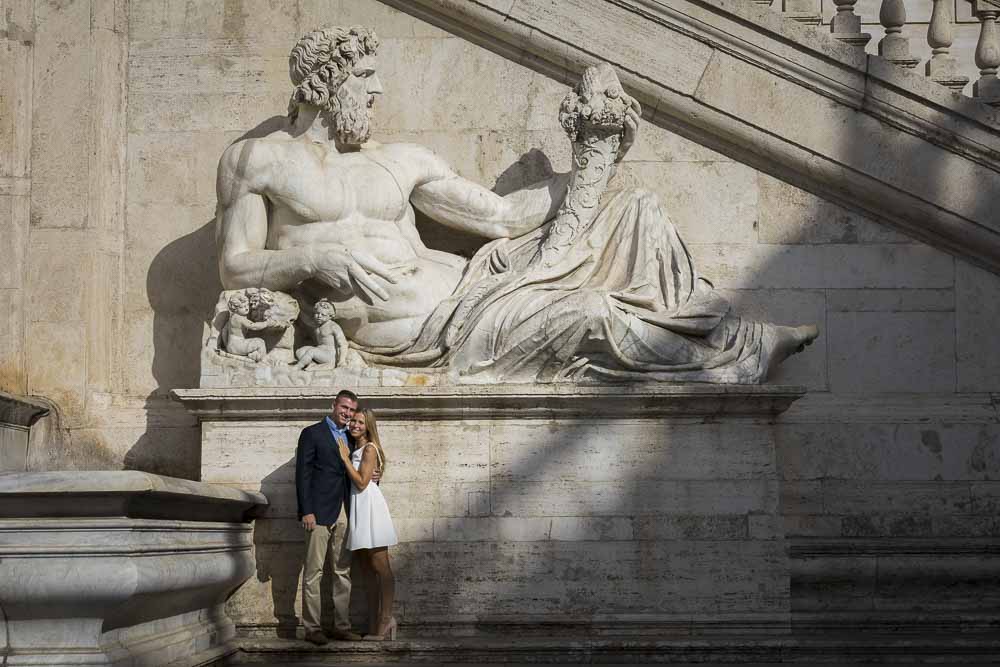 Engaged couple standing underneath a large marble statue