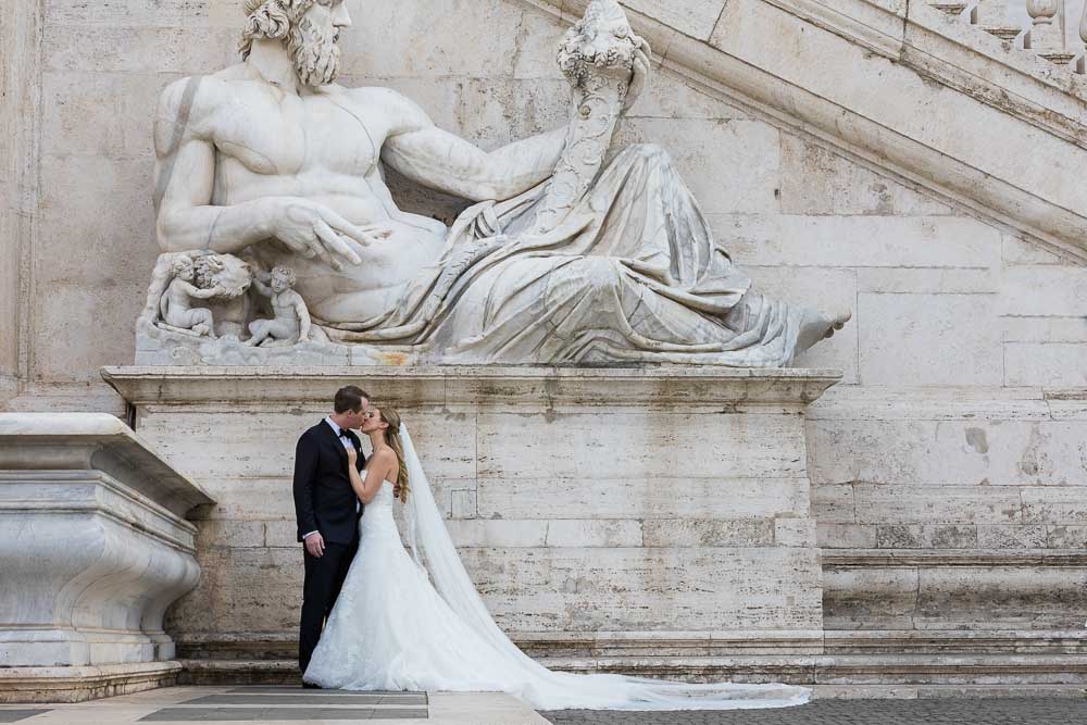 Married couple posing underneath an ancient roman statue in Piazza del Campidoglio in Rome