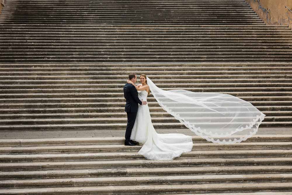 Wed pictures with bride and groom on the a scenic roman staircase with the veil up in the air