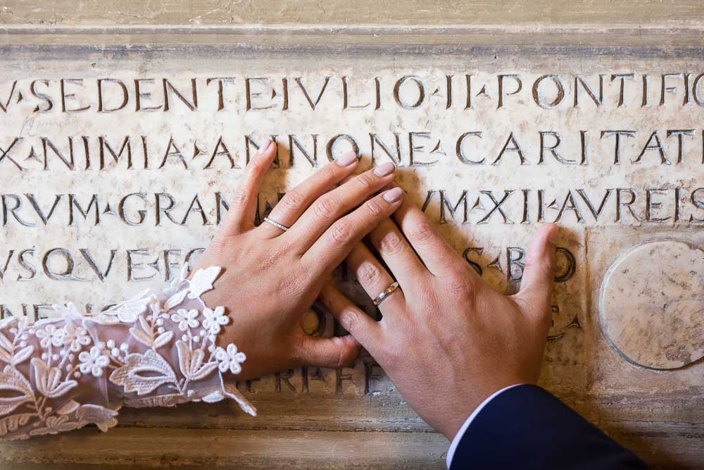 Hands closeup of the newlywed rings on ancient marble writing