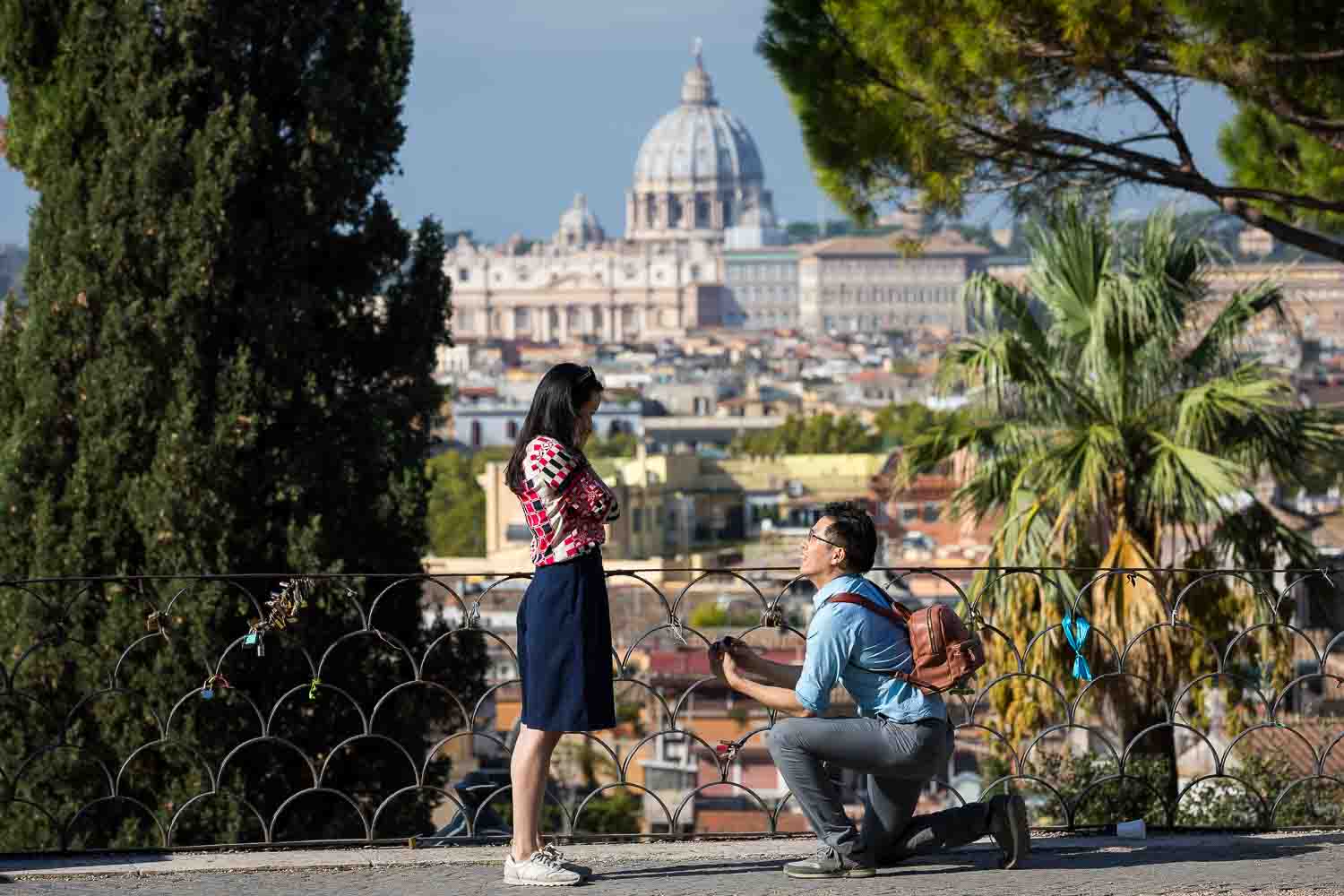 Man knee down proposing marriage before the scenic view of the Roman skyline and Saint peter's dome in the far distance