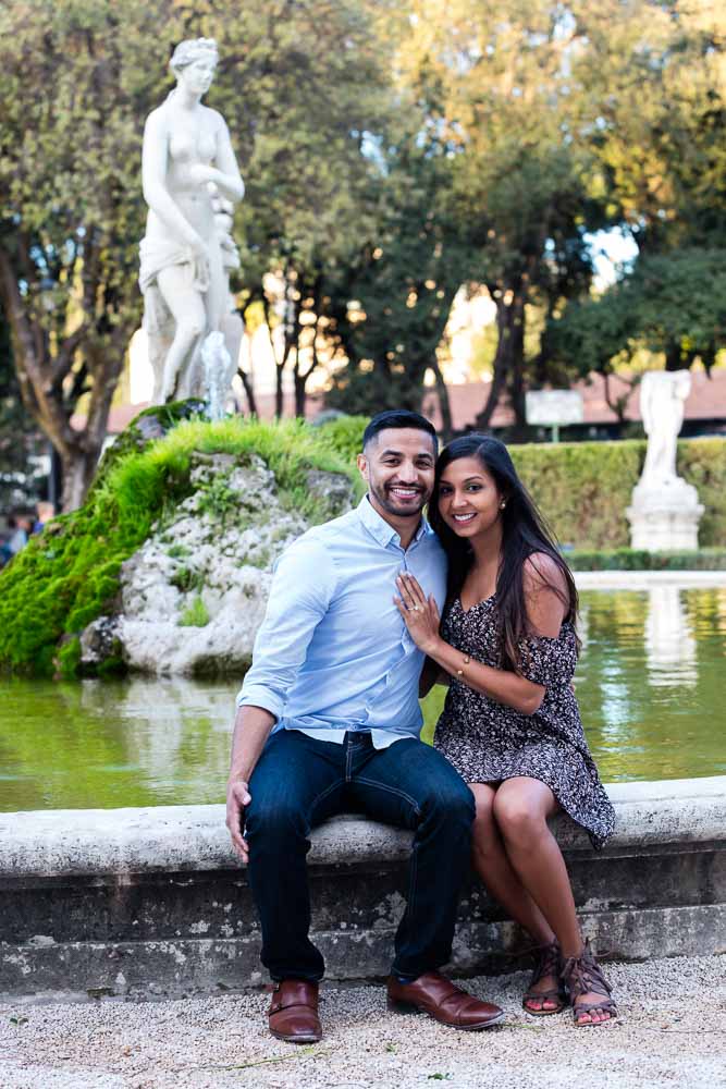 Portrait picture of a newly engaged couple sitting on the edge of a water fountain