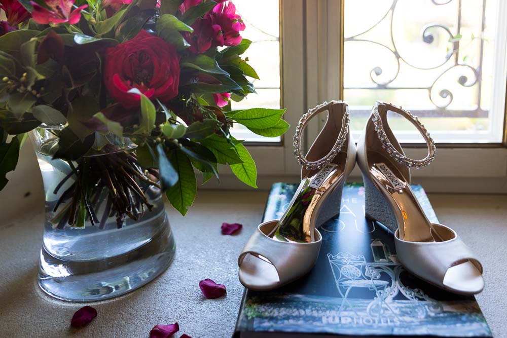 Bridal shoes photographed in window light next to red flowers