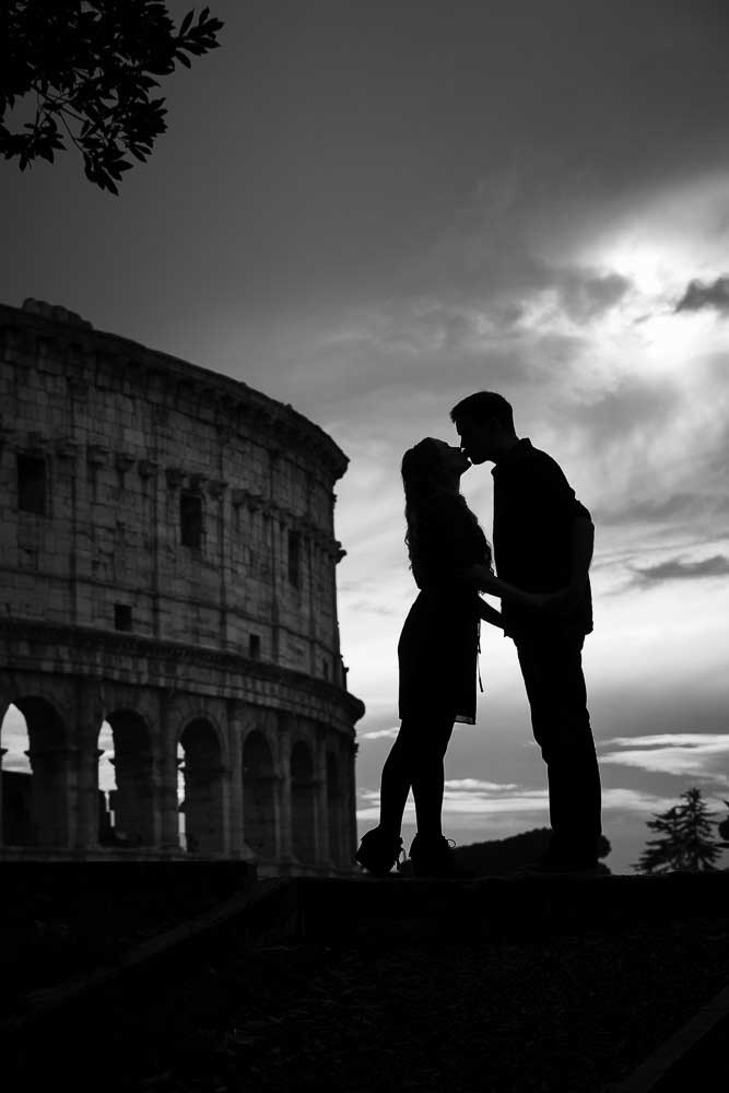 Italy Photoshoot. Just engaged kissing in front of the Coliseum in Rome Italy. Black and white fine art image by the Andrea Matone photography studio