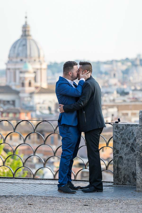 Same sex couple kissing before the roman rooftops