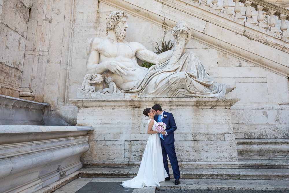 Wedding day photography of a couple standing underneath an ancient marble roman statue