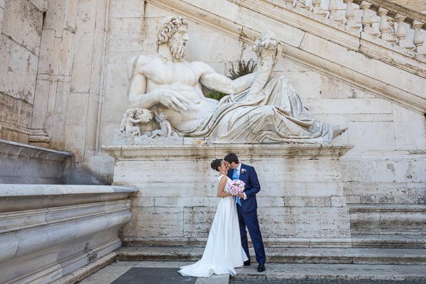 Couple just married kissing under and ancient roman marble statue