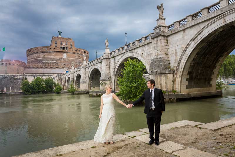 Holding hands down below the Tiber river with the Castle in the far distance