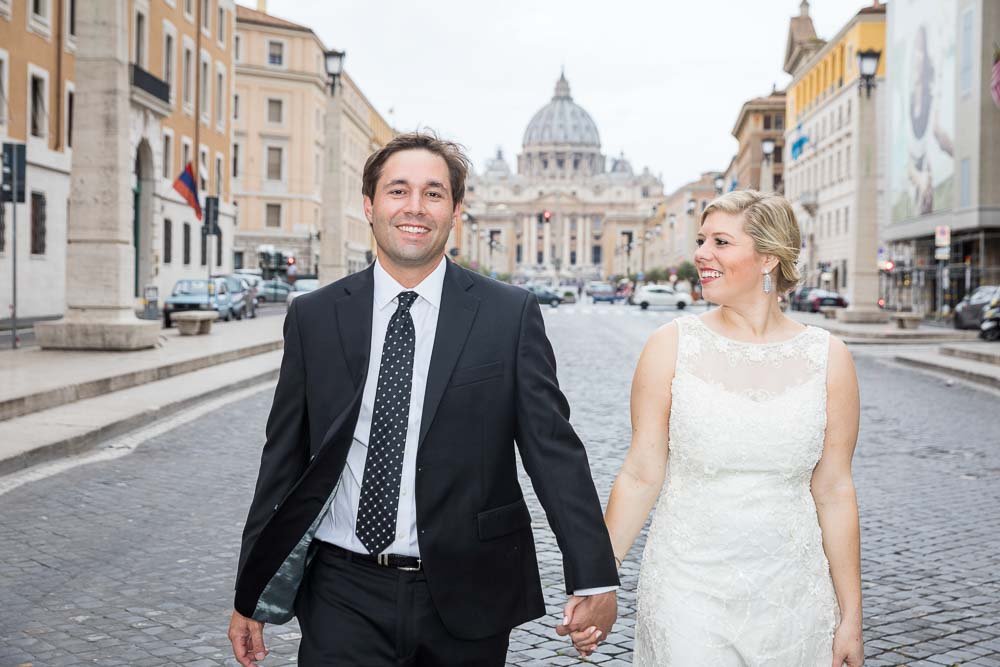 Bride and groom holdings hands and walking together in Via della Conciliazione with Saint Peter's in the background