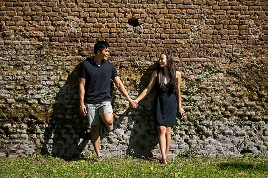 Couple holding hands and posing against an old roman wall