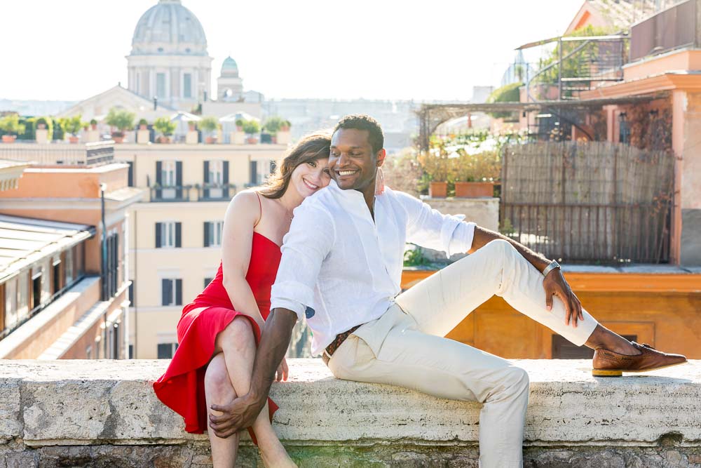 Couple posing sitting down on a ledge with the roman rooftops in the background