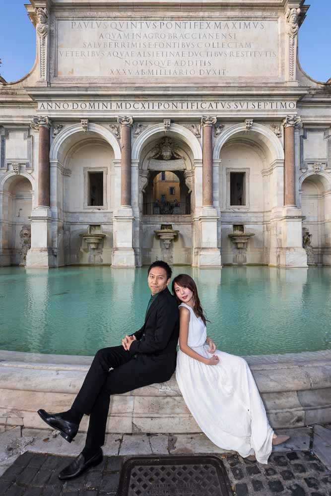 Portrait image of newlyweds sitting on the edge of the Fontanone water fountain