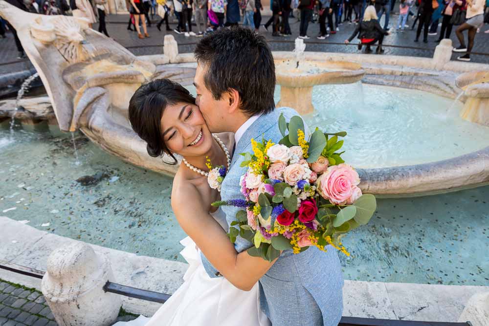 Married and in love taking photography by the Barcaccia water fountain holding the beautiful bouquet in one hand