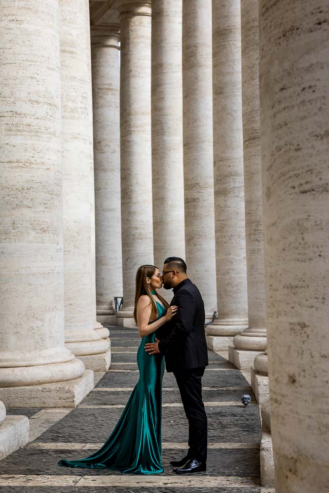 Couple standing kissing underneath the massive marble columns found in Saint Peter's square in the Vatican