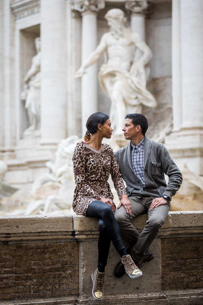 Portrait image of a couple sitting down in front of the statues in Piazza Fontana di Trevi