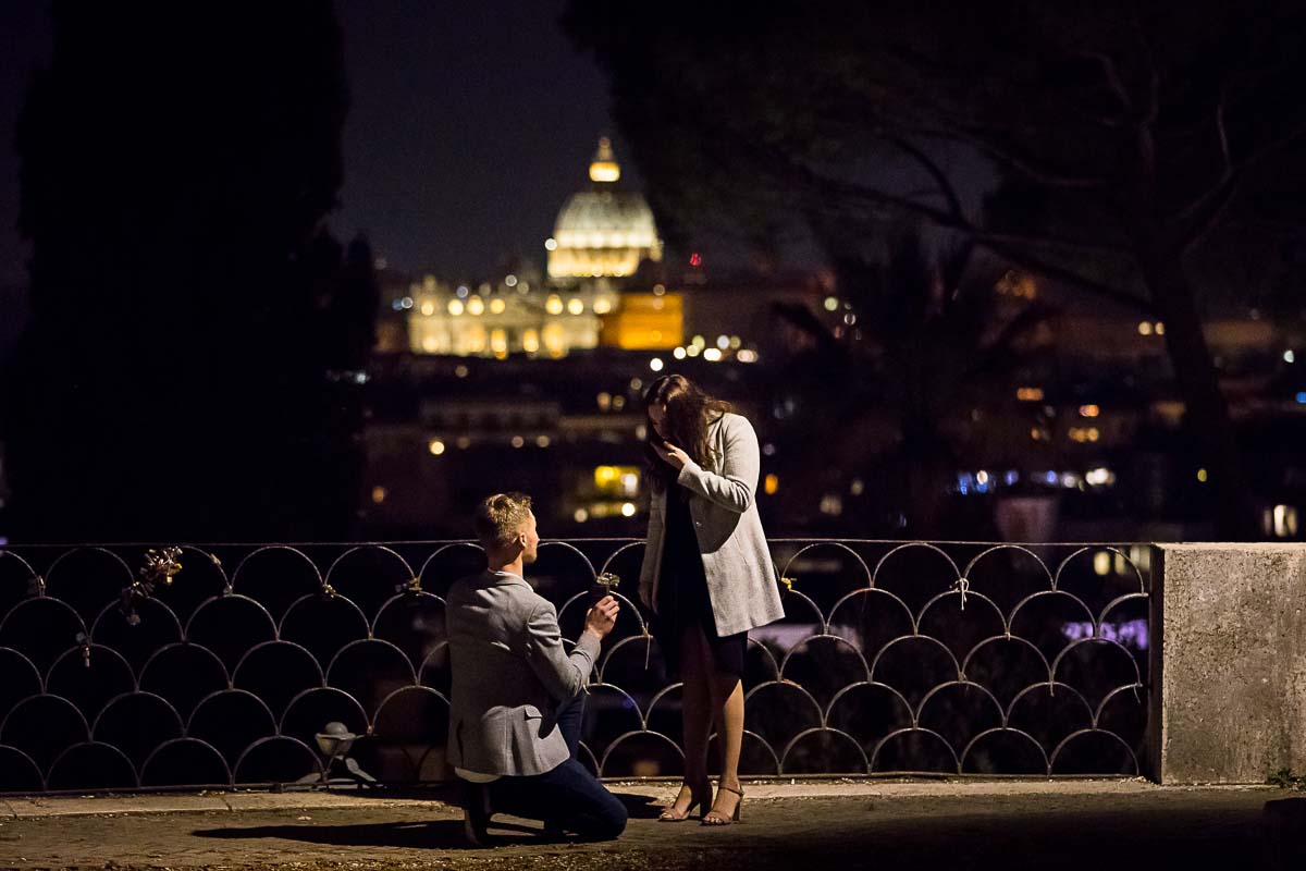 Man kneeling down proposing at night marriage before the sweeping night view of Rome and St Peter's dome in the far distance